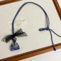 Close-up detail of a unique handbag stone pendant necklace featuring a black lace bow and cord. - Blue Bags Z-4431 / Blue