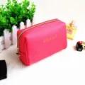 Detailaufnahme des rosafarbenen Kosmetiktäschchens mit goldenem Reißverschluss und Muster. - Fuchsia