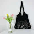 Detailansicht der schwarzen Häkel-Netz-Tragetasche mit Blumendekor an weißer Wand. - Schwarz