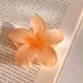 Close-up detail of a translucent jelly orange plumeria flower hair claw clip on book background. - Plumeria Orange-Tangerine