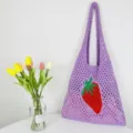 Detailaufnahme einer lila gestrickten Netztasche mit eingewebtem roten Erdbeermuster. - Violett