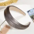 Vista detallada de diadema ancha de cuero con textura de serpiente y brillo metálico en soporte. - Café Oscuro