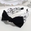 Close-up detail of the black and white floral headband with a chic bowknot and wide design. - Bow Floral Style / White