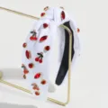 Detailansicht eines eleganten weißen Haarreifs mit roten Strasssteinen und Kirschen. - Kirsche