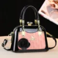 Dettaglio borsa a mano in pelle verniciata nera con toppa rosa, ferramenta dorata e ciondolo. - Rosa
