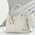 Elegante borsa in pelle beige con ciondolo floreale, doppi manici e tracolla elegante. - Bianco