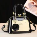 Vista dettagliata della borsa nera lucida e beige con dettagli dorati e decorazione floreale. - Giallo