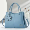 Dettaglio di borsa in pelle blu elegante con delicato ciondolo a fiore e finitura testurizzata. - Blu