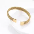 Gros plan détaillé du bracelet manchette en acier inoxydable doré avec des embouts carrés. - Or