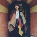 Detailed view of the stylish geometric color-blocked knitted cape in cozy vintage street scene. - Classic Color Block - Orange