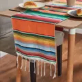 Close-up detail of colorful Mexican striped table runner with white fringe on wooden table. - Mexican Blanket - Orange Tones