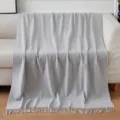 Cozy light gray throw blanket with fringe draped on beige sofa, soft home decor scene. - Solid Color Throw Blanket - Grey