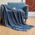 Detailed view of blue knitted blanket with tassels draped on modern sofa in home setting. - Navy Blue