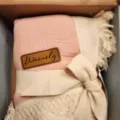 Close-up of pink muslin baby swaddle blanket detail featuring soft fringe and branded leather tag. - 68x85cm-200g / Pink