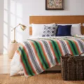 Detailed view of handmade woven Mexican throw blanket on bed, geometric stripe pattern. - 130x170cm / MC Green Orange Red
