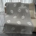 Grey knitted plush football pattern blanket draped on sofa, cozy fleece throw for home decor. - Rugby Ball / Off-White