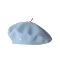Hellblaue Wollbarette mit rotem Stiel oben und einem Knopf an der Seite. Detailaufnahme. - Blau