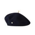 Detailansicht der dunkelblauen Wollbaskenmütze mit oberem Stab und goldenem Metalllogo. - Marineblau