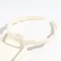 Gros plan détail du serre-tête ondulé en plastique minimaliste de couleur beige unie. - Blanc Cassé