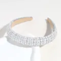 Close-up detail of the luxury baroque rhinestone and pearl padded headband surface texture. - White