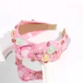 Detailaufnahme eines rosa geknoteten Haarreifs mit bunten Harzherzen und funkelnden Strasssteinen. - Rosa