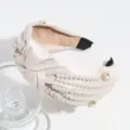 Detailopname van een chique beige satijnen haarband met knoop, versierd met parels en strass. - Beige