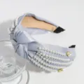 Gedetailleerde close-up van de brede satijnen haarband met knoop, parels en strass steentjes. - Lichtblauw