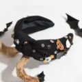 Close-up detail of the black wide knotted rhinestone headband featuring festive Halloween charms. - Black