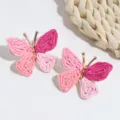 Close-up detail of pink straw woven butterfly earrings with gold metallic frame, bohemian style. - Pink Purple Butterfly
