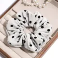 Detailed close-up of grey plush polka dot hair scrunchie in wooden tray with pearls. - Off White