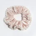 Primo piano dettaglio di un morbido scrunchie di velluto rosa con perle bianche eleganti. - Kaki