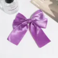 Closeup of a purple satin bow hair clip with elegant ribbon tail and secure clip detail. - Purple