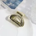 Close-up van een moderne geometrische gouden metalen haarklem op een wit bordje. - Gouden Holle Halve Cirkel