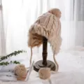 Beige Strick-Trapperhut mit Plüsch-Kunstfellbesatz, warme Wintermütze mit Ohrenklappen und Bommeln. - M (56-58cm) / Verdrehter Stil / Beige