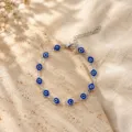 Macro view of a silver chain bracelet featuring blue Turkish evil eye charms on stone. - Dark Blue Silver