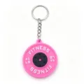 Close-up detail of the pink barbell plate keychain, showing the textured fitness design clearly. - Pink