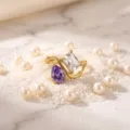 Closeup view of a gold-plated titanium steel ring featuring a purple and clear gemstone design. - Size 5 / Birthstone - April
