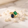 Elegant asymmetrical dual-stone ring with green and blue crystals in gold finish. - Birthstone - May