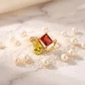 Detailed close-up of the elegant gold-plated dual-stone ring styled with pearls on sand. - Birthstone - July