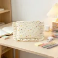 Close-up of a beige floral cosmetic bag with cute ruffled edges on a wooden desk. - Little Floral