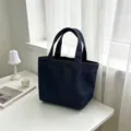Detailed view of dark blue denim tote bag, minimalist style mini handbag on white desk setting. - Dark Blue Denim