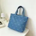Blue denim tote bag detail featuring white embroidered bow patterns and vertical stitching. - Light Blue Bow