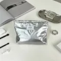 Dettaglio borsa cosmetica impermeabile lucida argento con finitura metallica ed etichetta. - Argento