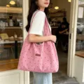 Detail view of a pink suede polka dot tote bag worn by a model in a cozy cafe setting. - Pink