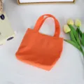 Detail view of a vibrant orange mini nylon tote bag styled with fresh tulips on white background. - 21*6*27cm / Orange