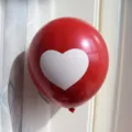 Close-up detail of a red latex balloon featuring a printed white heart decoration - Red with White Hearts