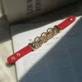 Nahaufnahme eines leuchtend roten Lederarmbands im Punk-Stil mit groben goldfarbenen Kettengliedern - Punk-Stil Ketten-Design / Rot