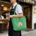 Vista detallada del bolso tote de lona verde con cerdito bordado llevado en el café. - Verde