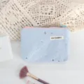 Close-up view of light blue cosmetic pouch featuring silver star sequins and pink zipper. - Blue