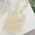 Vue détaillée du sac cabas brodé en dentelle blanche sur table propre avec accessoires. - Sac à main